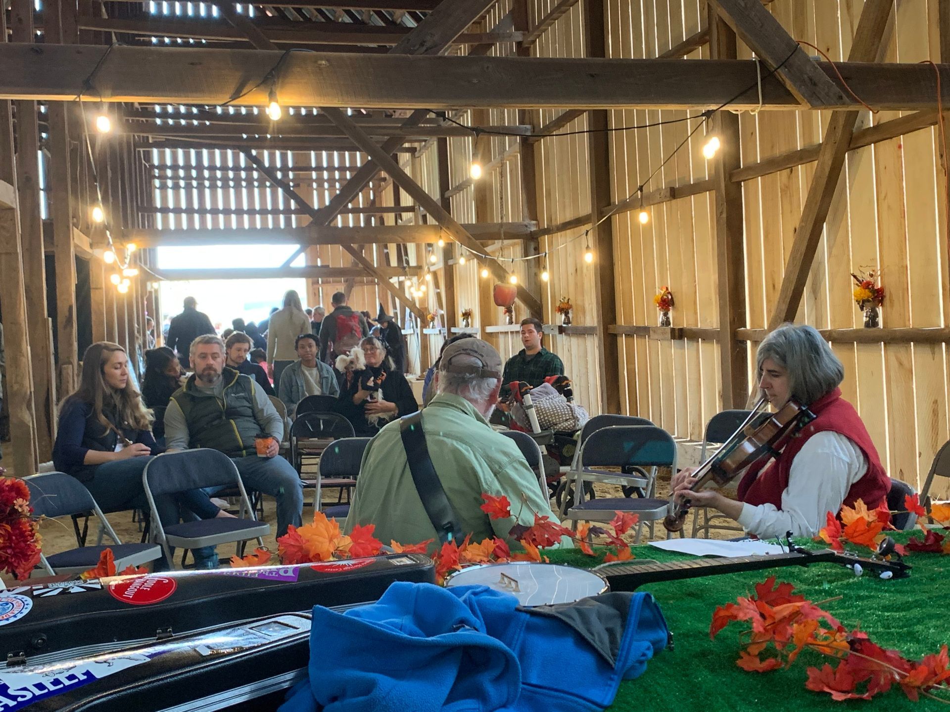 Indoor gathering in a wooden hall with seated people, candles, and a blue-covered table decorated with flowers.