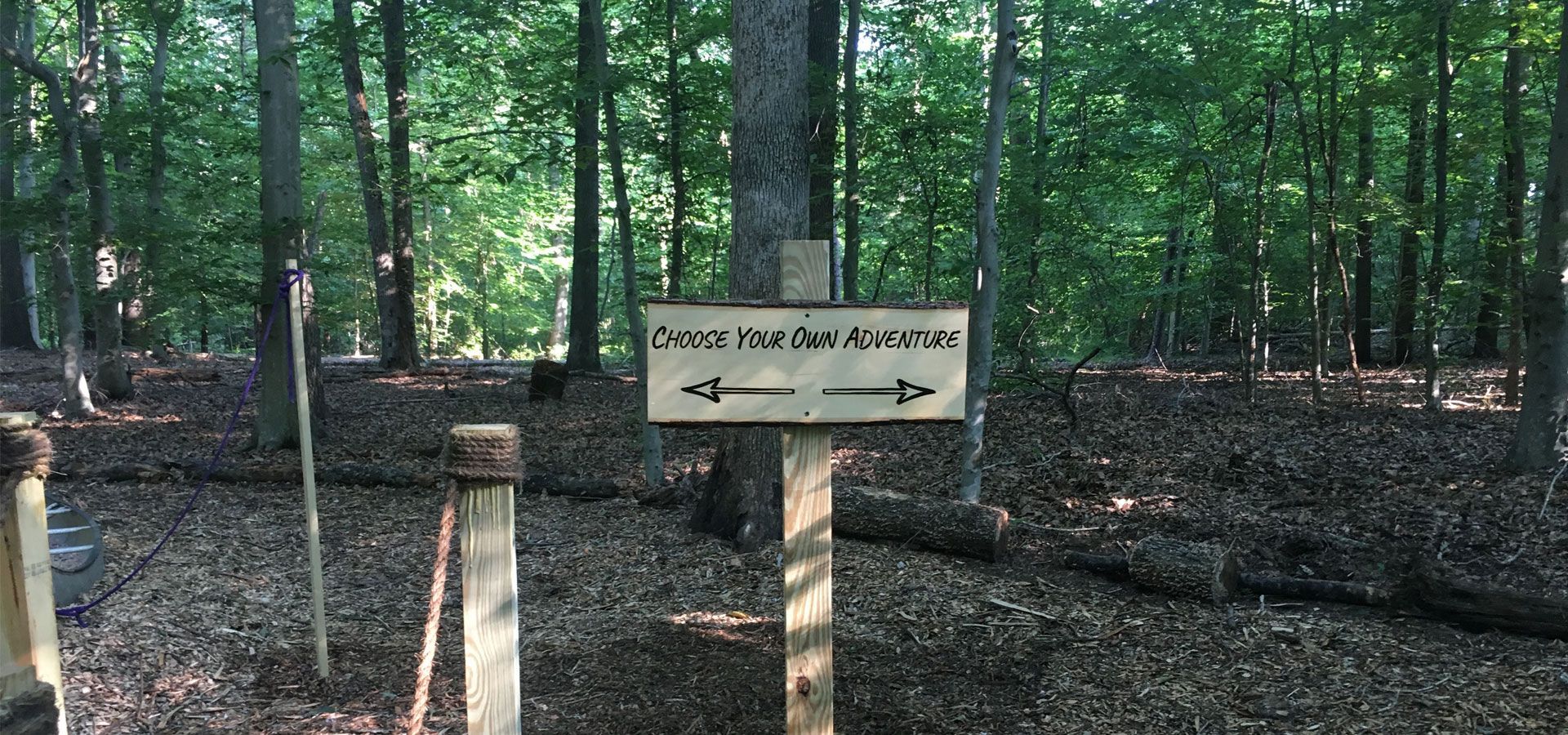 Wooded trail entrance with a sign reading “Forest Park Nature Center” in front of trees and leaf-covered ground