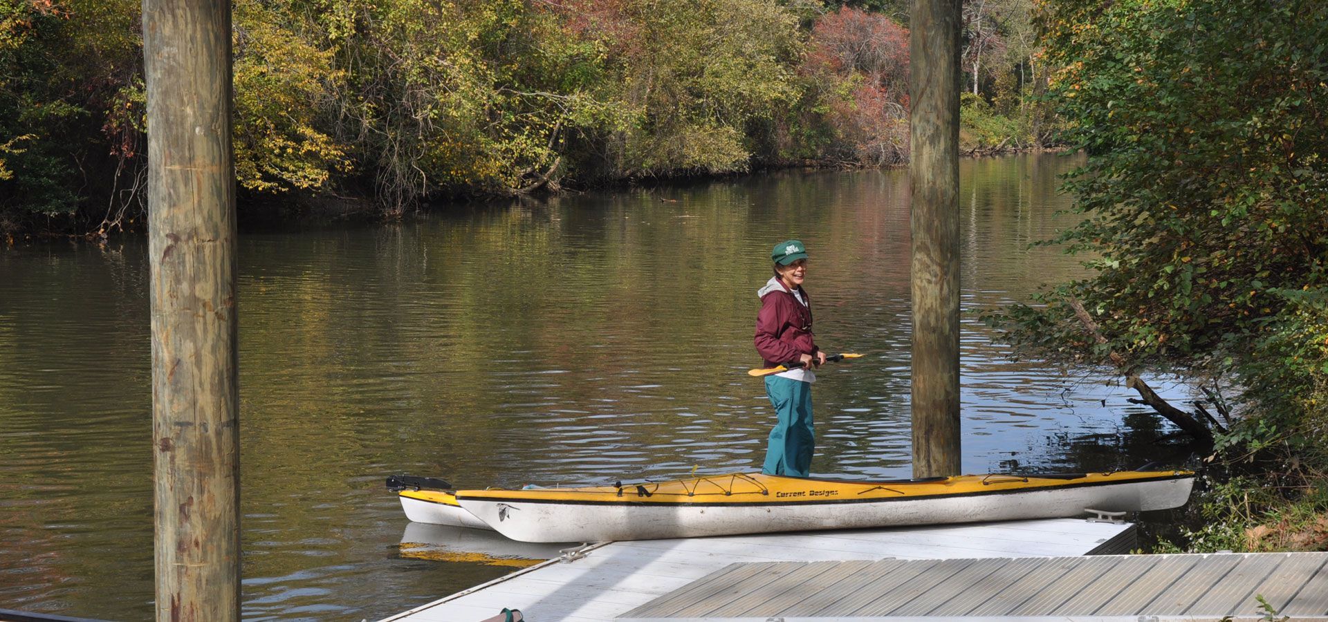 Person standing on a canoe by a calm river in a wooded area