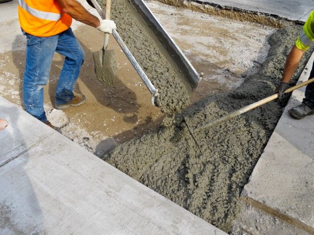 Skilled team member pouring wet concrete into a prepared form for a residential patio project.