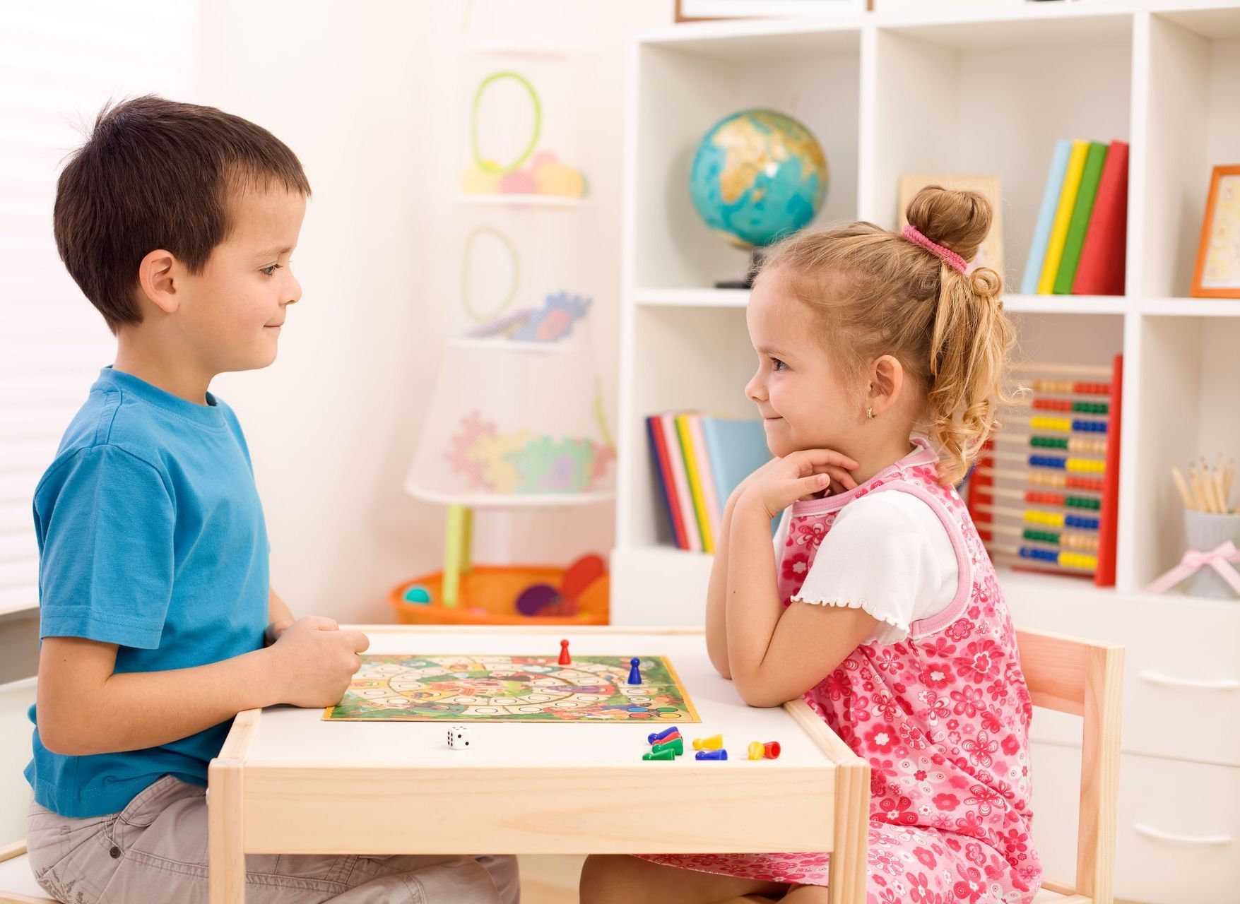 A boy and girl are sitting at a play table looking at each other.
