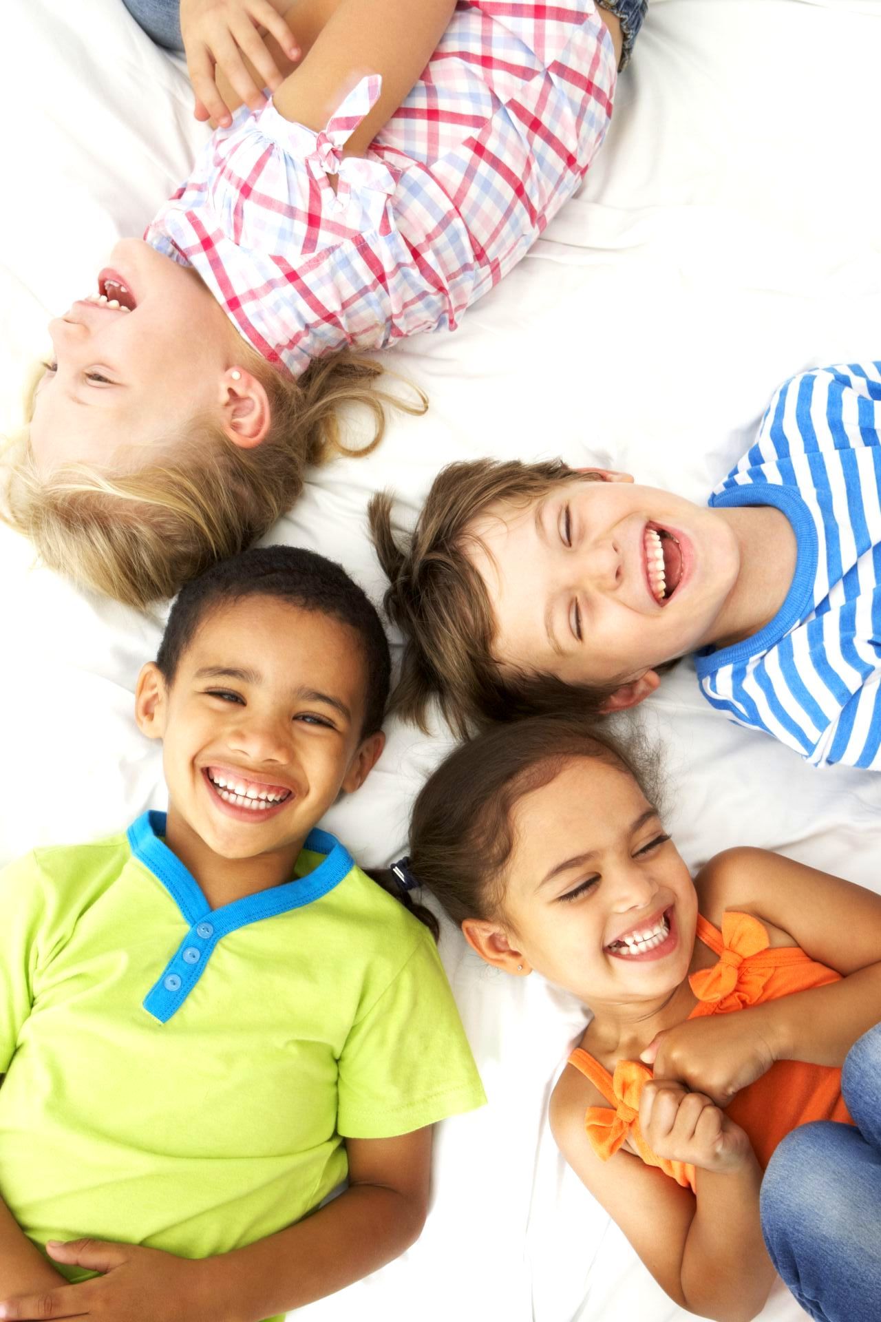 A group of smiling, laughing children are lying down in a circle.