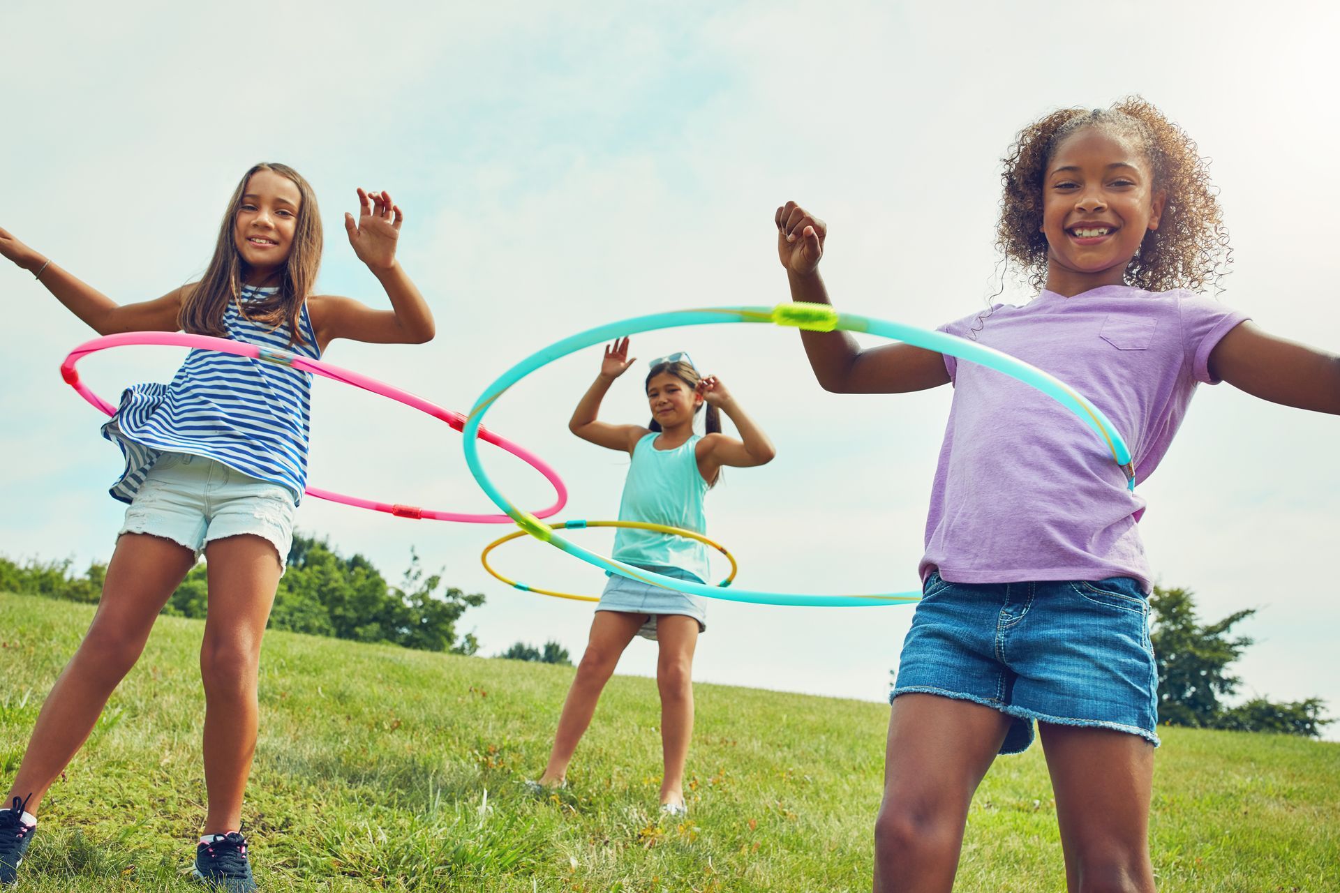 Three girls on in a park using hula hoops.