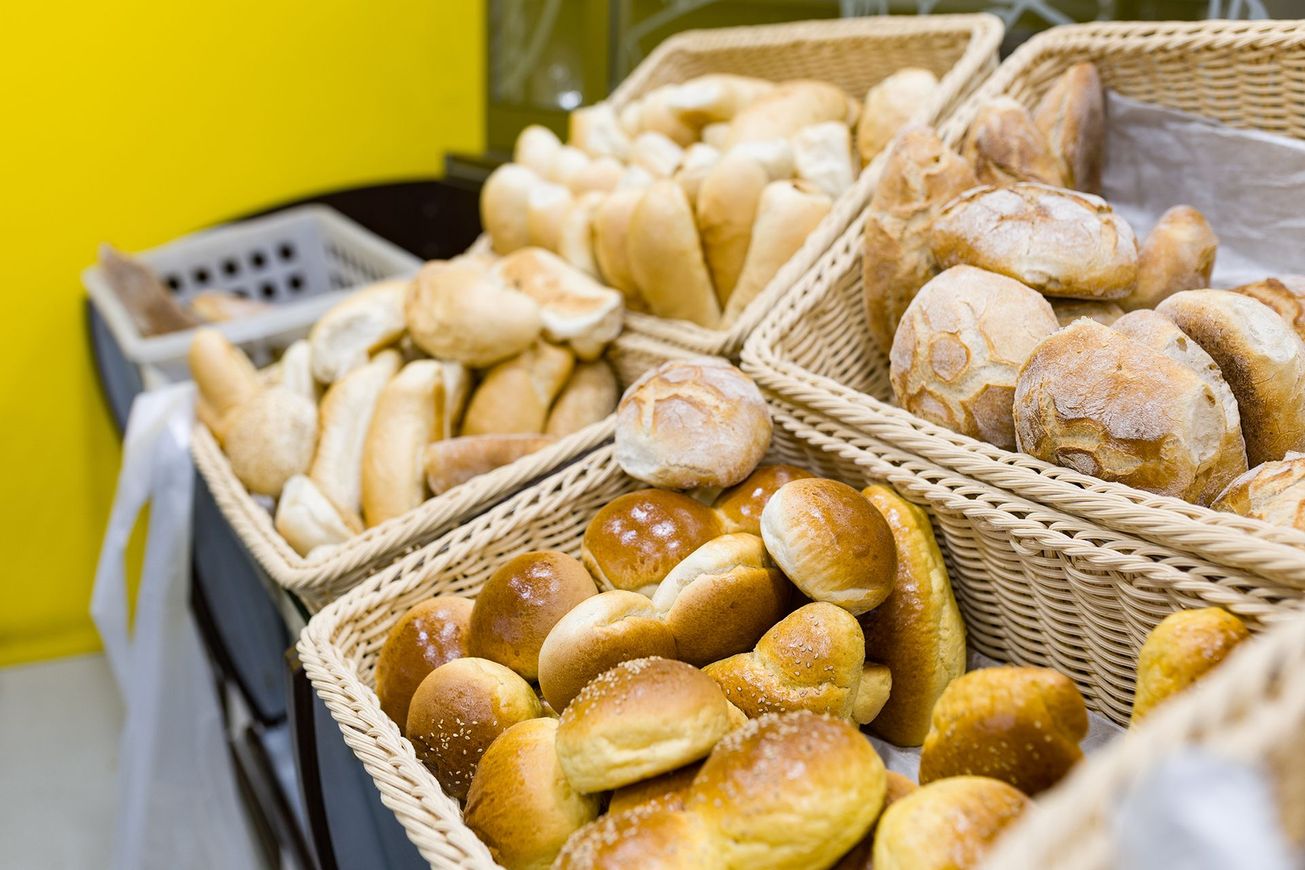 Assortimento di pagnotte e panini freschi in cesti di vimini al bancone di una panetteria.