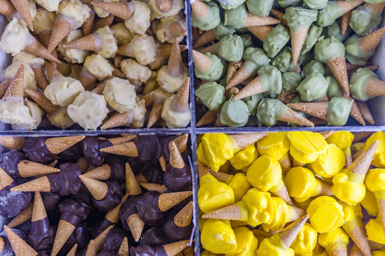 Macarons e pasticcini assortiti disposti su vassoi di metallo al bancone di una pasticceria.