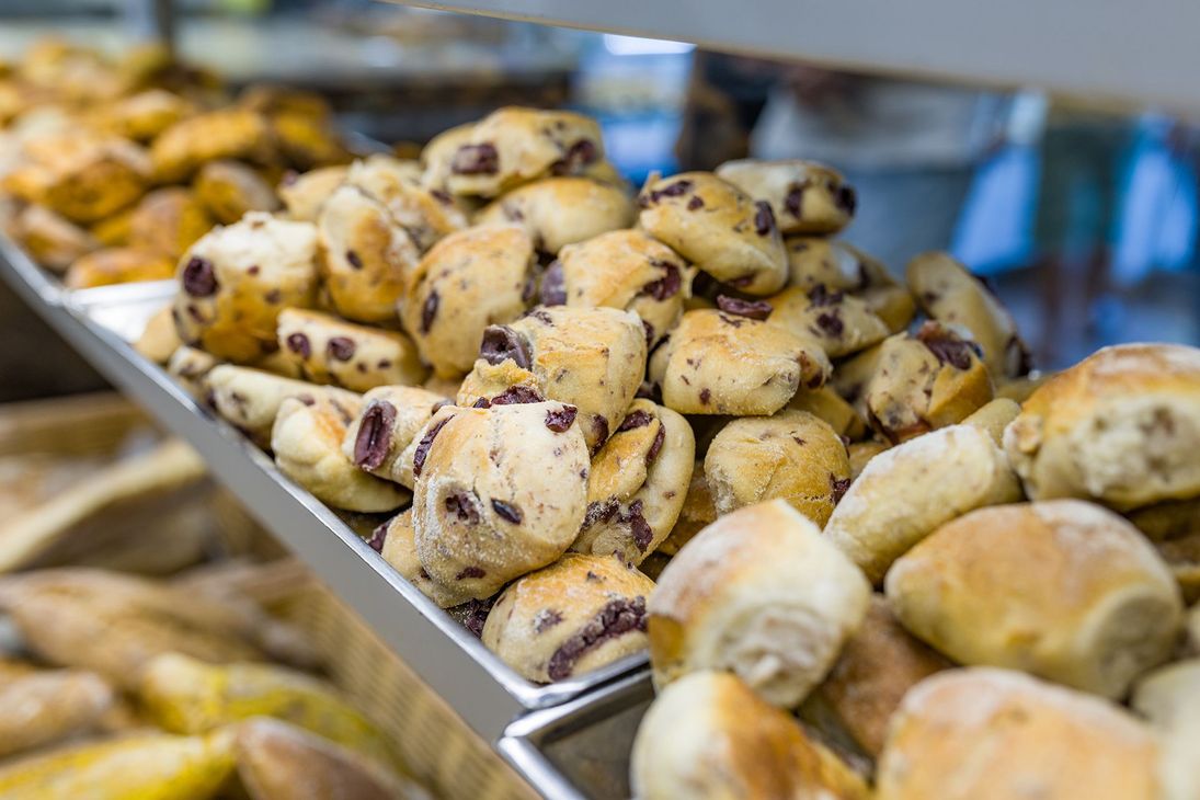 Vassoio di prodotti da forno assortiti, tra cui girelle con gocce di cioccolato, esposto in una vetrina da pasticceria.