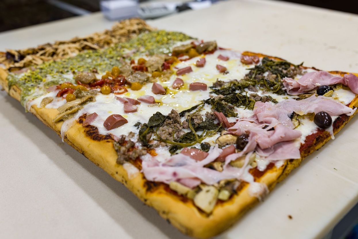 Pizza rettangolare con formaggio fuso, erbe aromatiche e prosciutto a fette, servita su un vassoio.