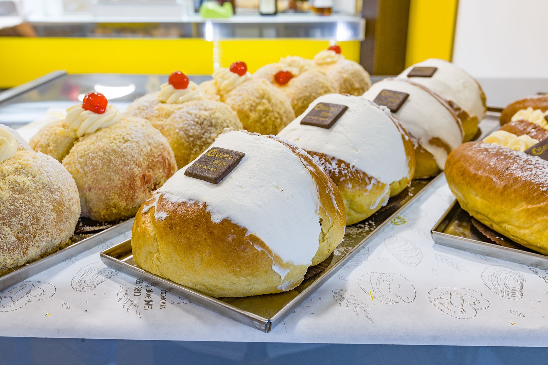 Pasticcini e dessert ripieni di crema disposti su un vassoio da pasticceria, con decorazioni di zucchero a velo e cioccolato.