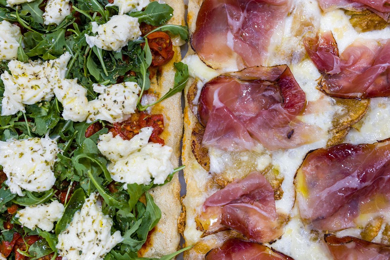 Due pizze gourmet: una con rucola, ricotta e pomodori secchi; l'altra con prosciutto e formaggio fuso.