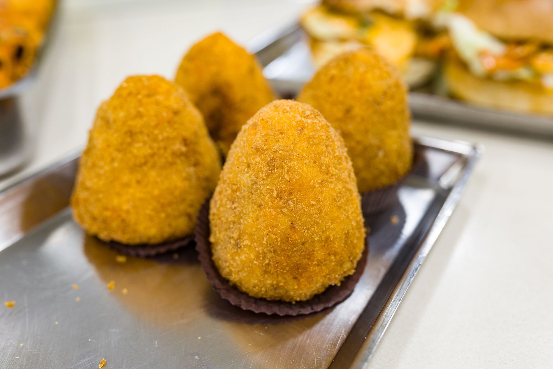 Crocchette dorate fritte su un vassoio di metallo, con altri antipasti sfocati sullo sfondo.