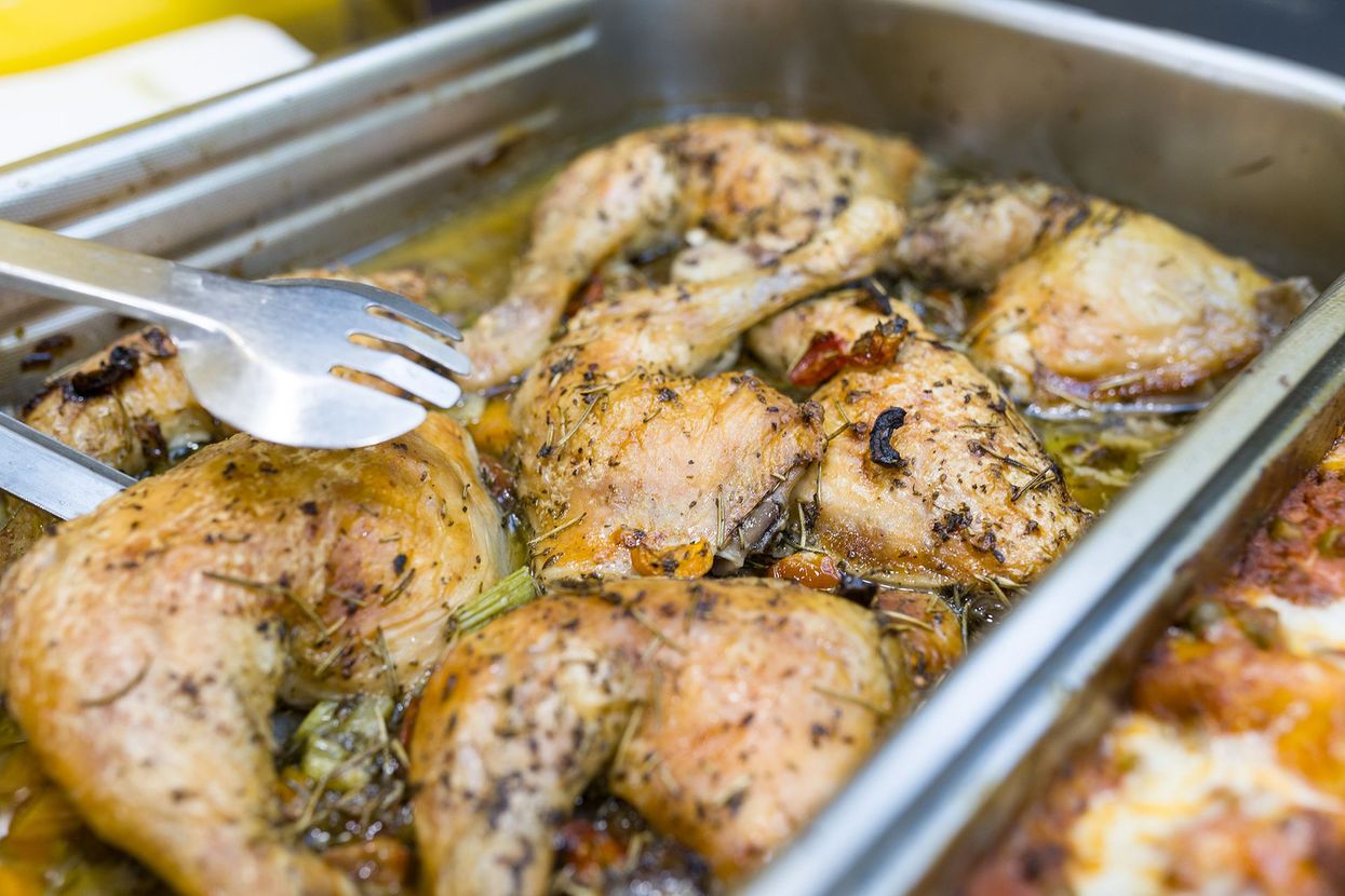 Pezzi di pollo arrosto in un vassoio di metallo, girati con delle pinze.