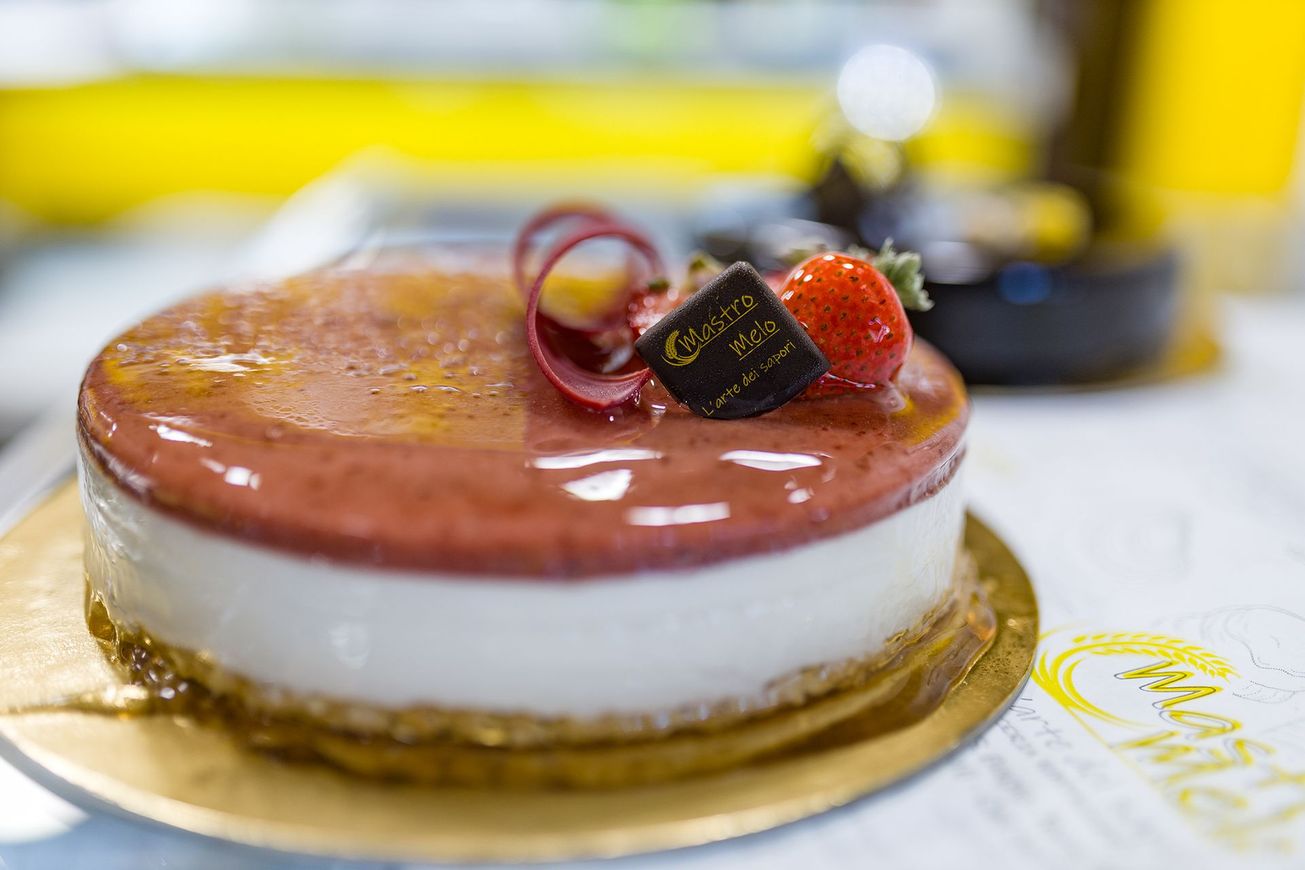 Torta lucida alla mousse di fragole su un vassoio dorato con guarnizione di frutta.