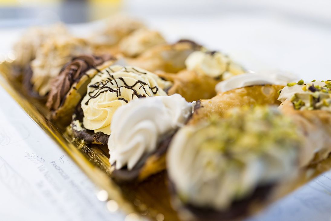 Cannoli assortiti con glassa al cioccolato e guarnizione al pistacchio, serviti su un vassoio.