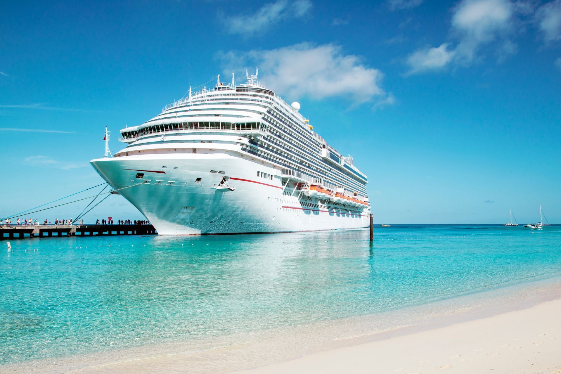 Large white cruise ship docked near a turquoise beach under a clear blue sky