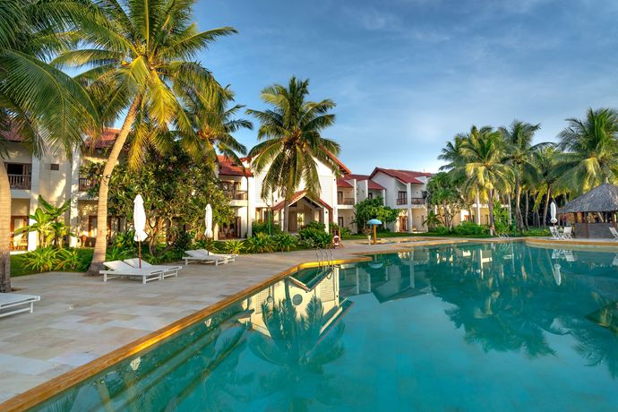 Resort pool beside palm trees and white lounge chairs, with tropical villas reflected in turquoise water