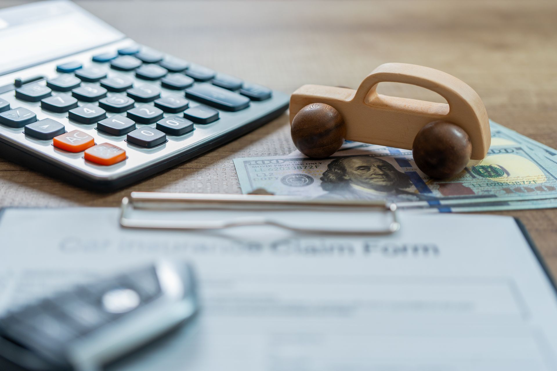 Calculator, wooden car, money, and claim form, suggesting car financing or insurance.