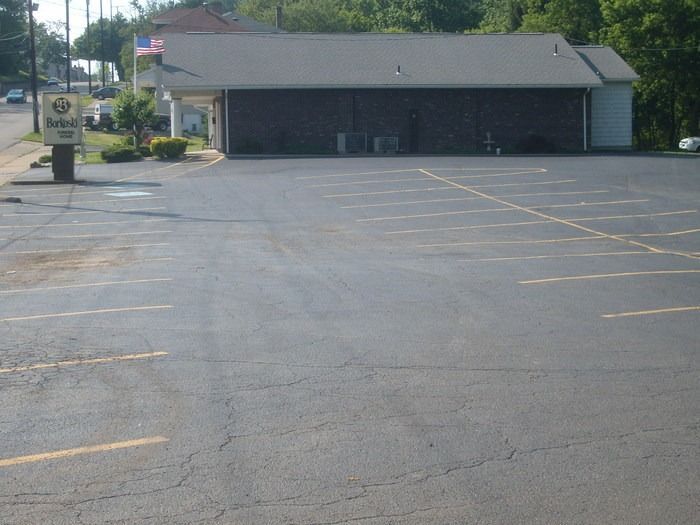 Empty parking lot in front of a small building with a U.S. flag and sign by the road.