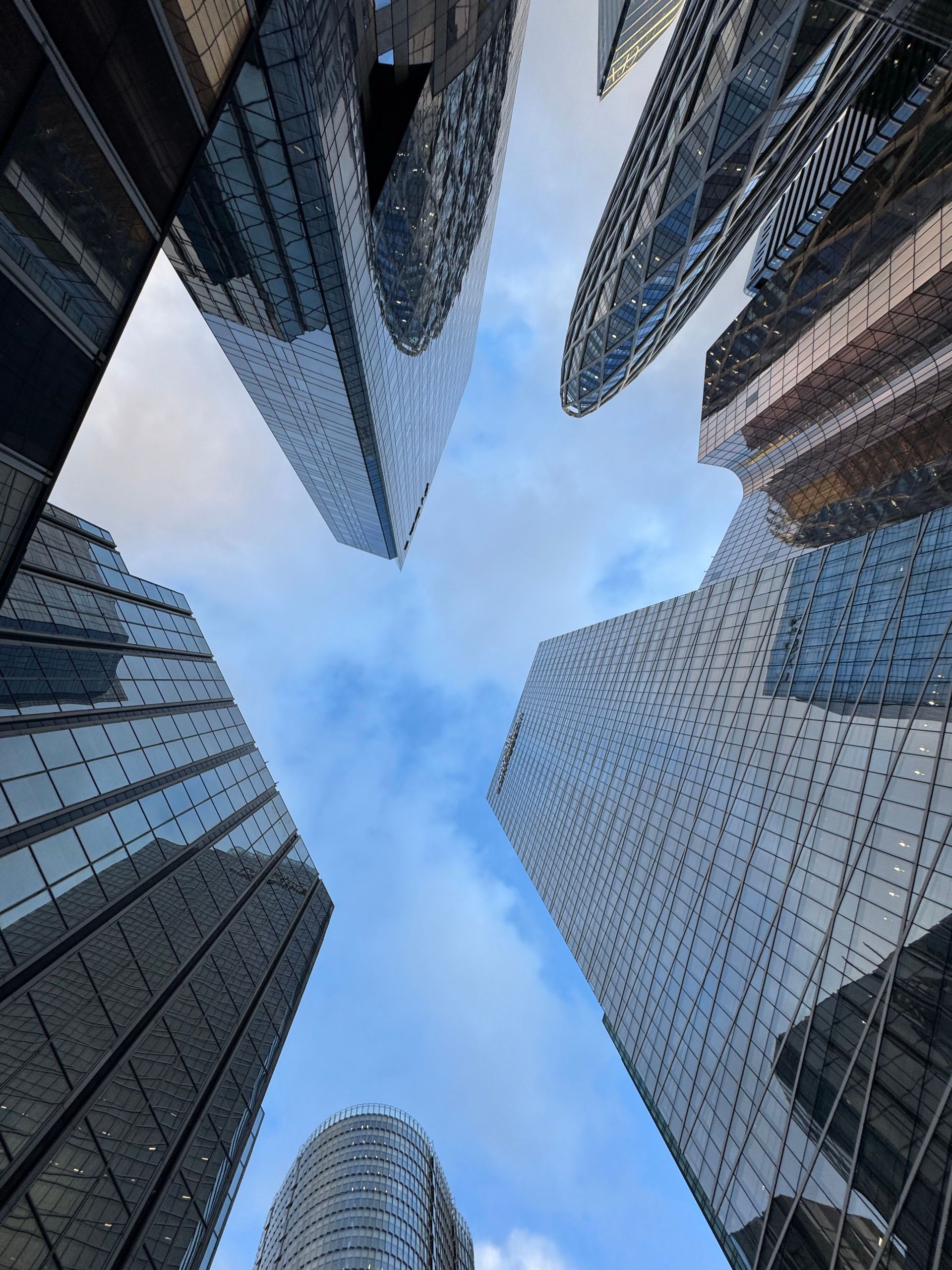 Looking up between tall glass skyscrapers framing a blue sky in the center