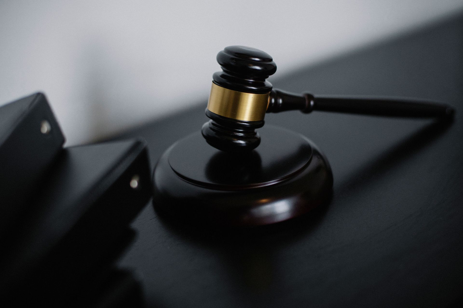 Judge’s gavel on a dark wooden block beside a black folder on a table