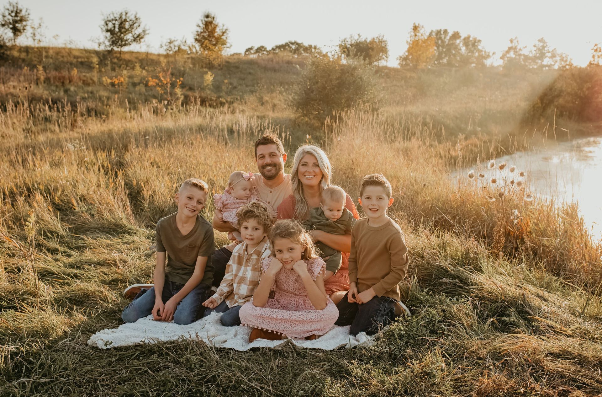 A family is sitting on a blanket in a field next to a river.
