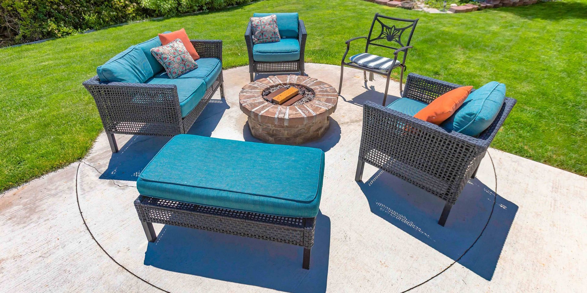 Outdoor patio seating with teal cushions around a fire pit on a paved backyard patio.