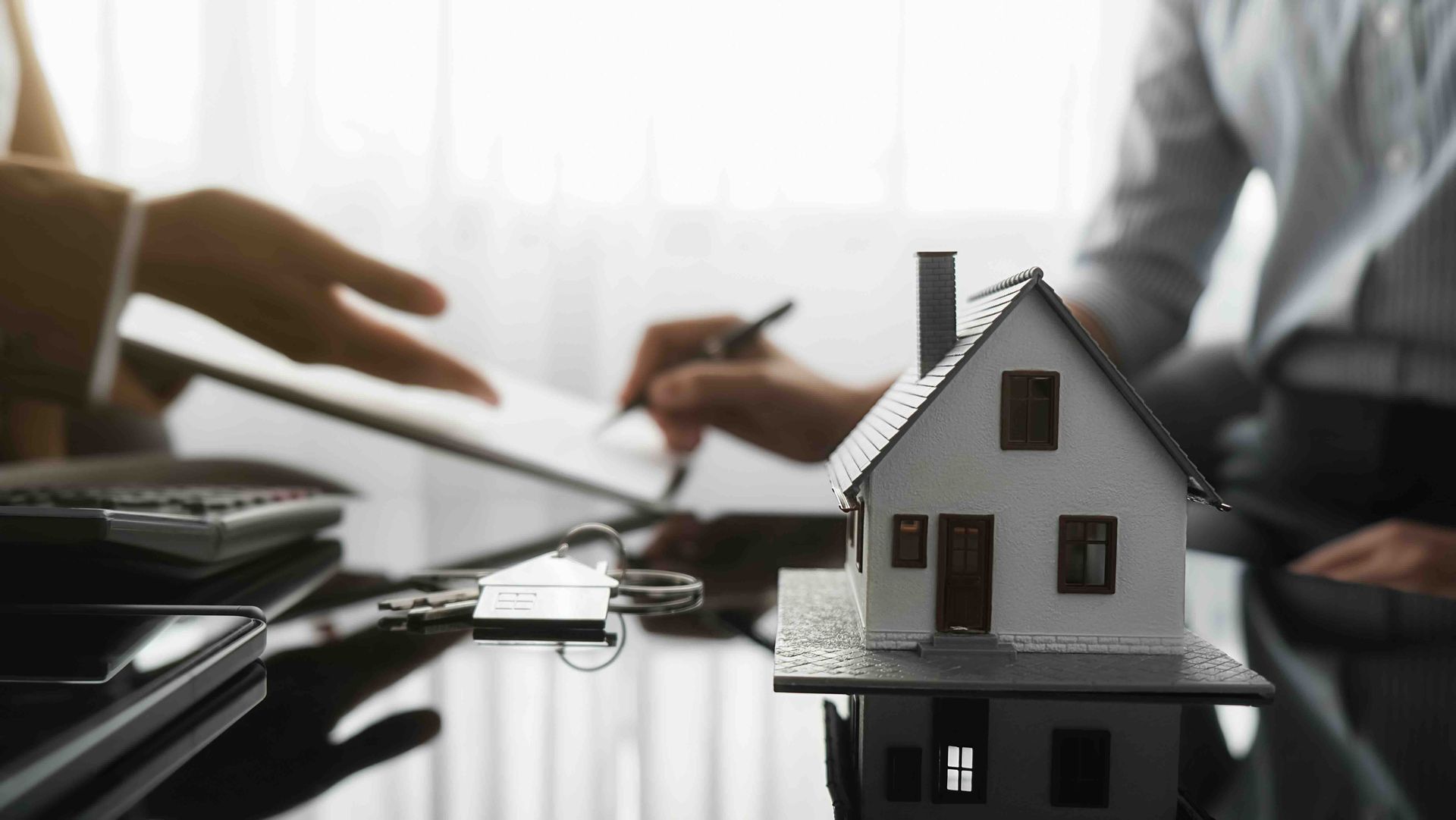 a man is signing a document next to a model house on a table.