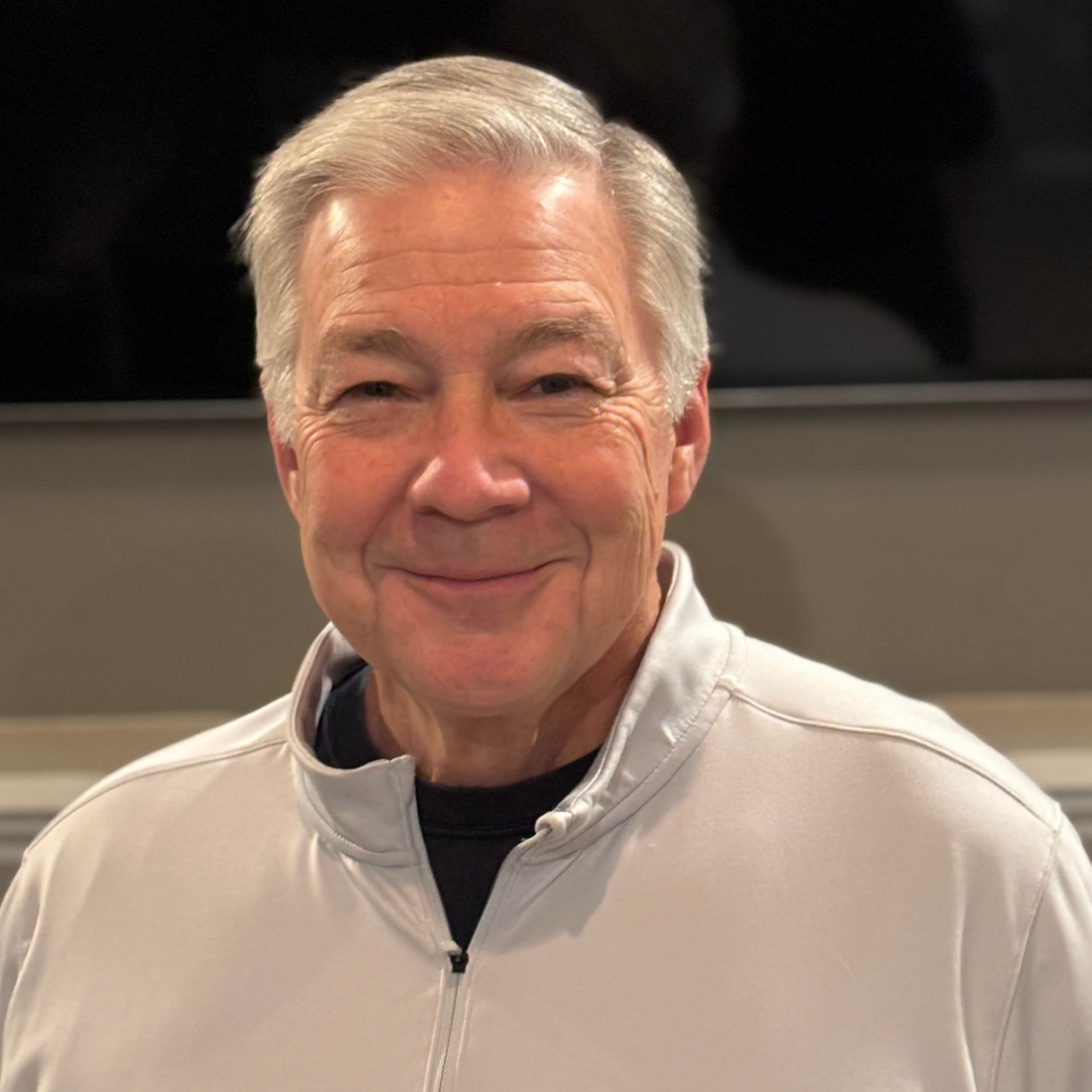 Fred Smith in a light gray zip-up jacket against a dark background