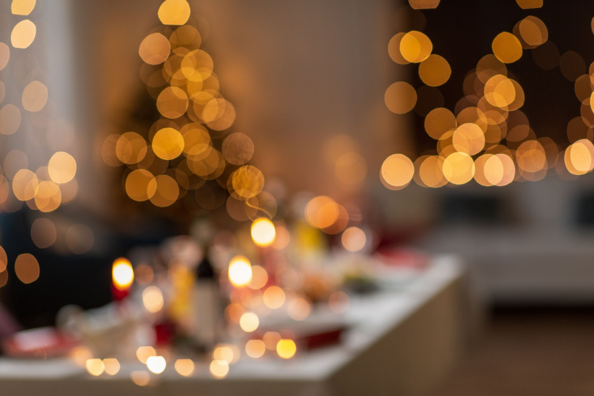 Warm, softly lit dining table with candles and blurred golden holiday lights in the background