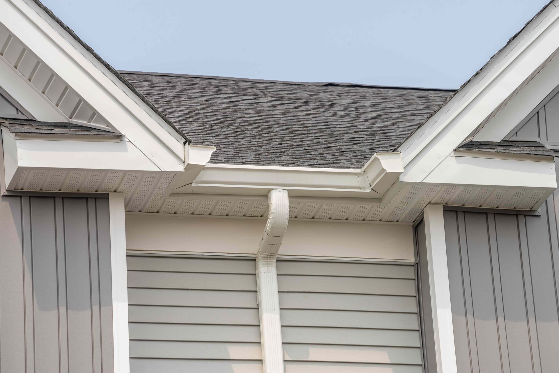 Damaged gutter hanging between white house roof gables with missing shingles