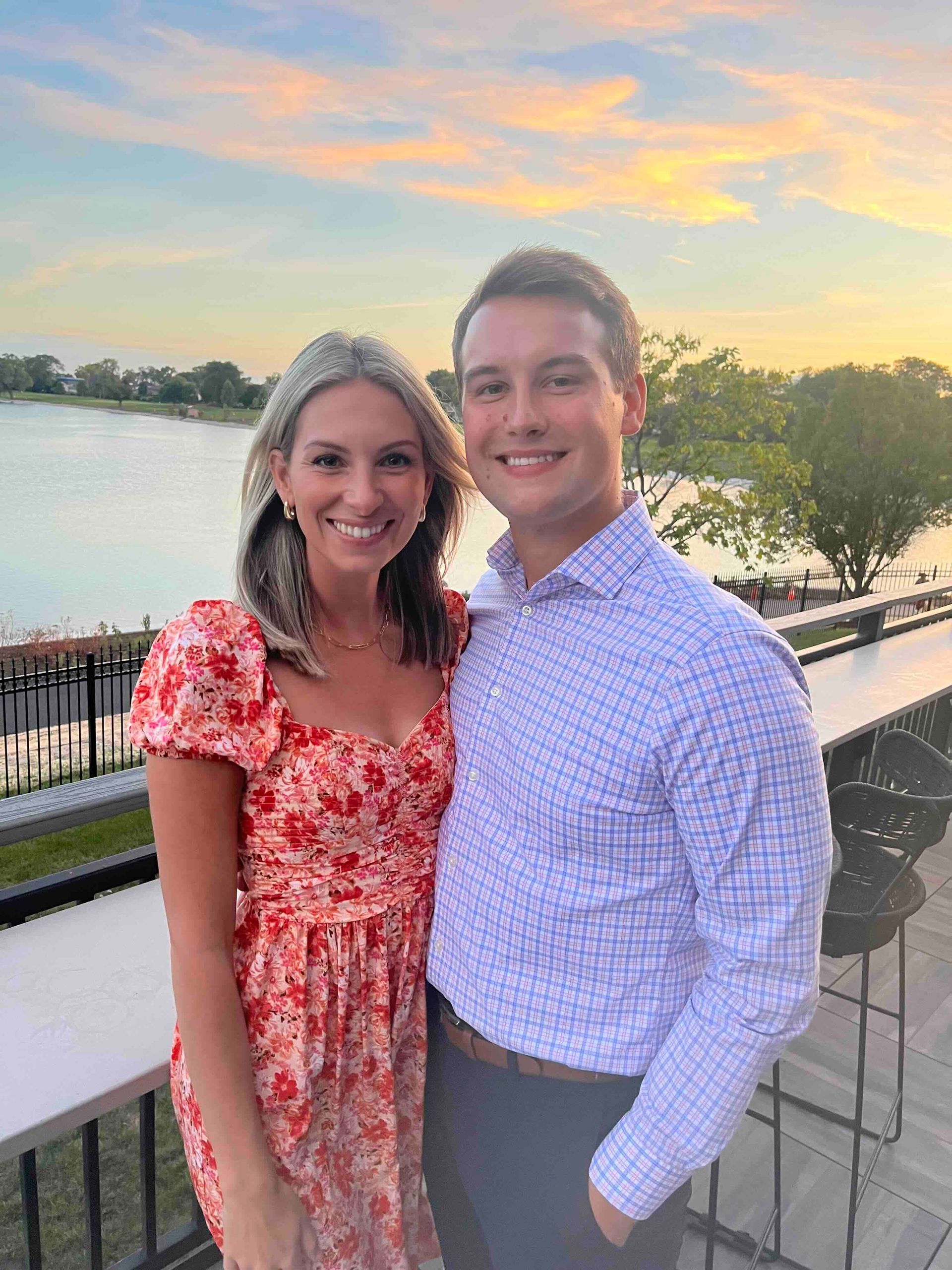 A man and a woman are posing for a picture on a balcony overlooking a lake.