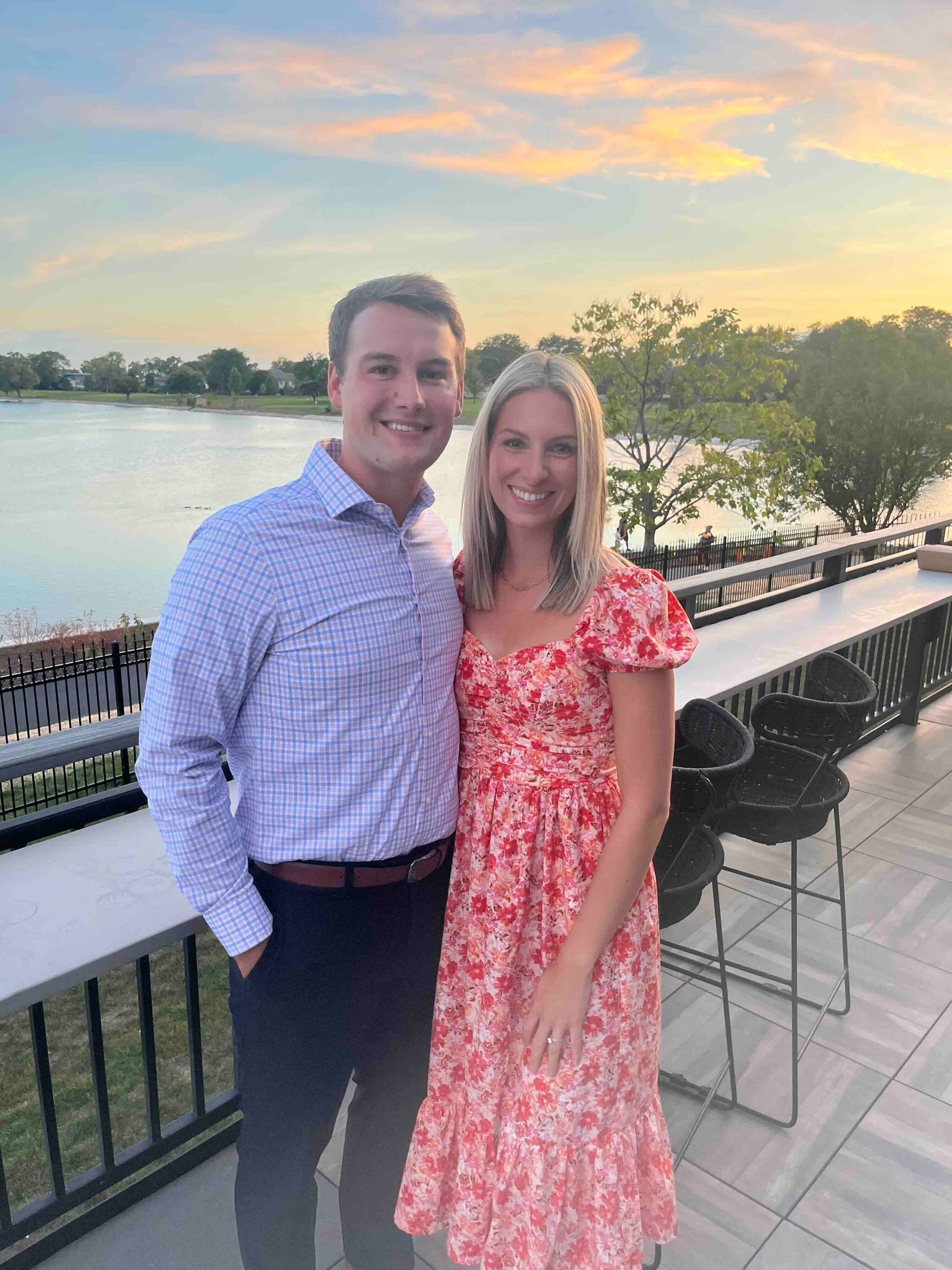 A man and a woman are standing next to each other on a balcony overlooking a lake.