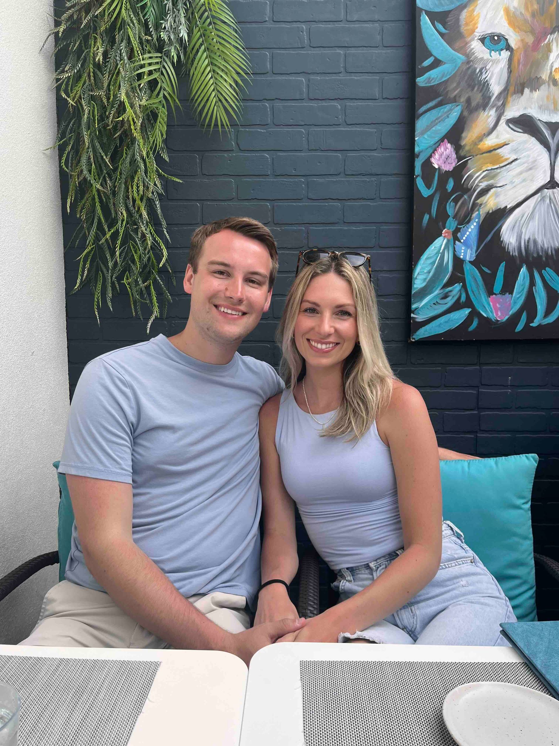A man and a woman are sitting at a table in front of a painting of a lion.