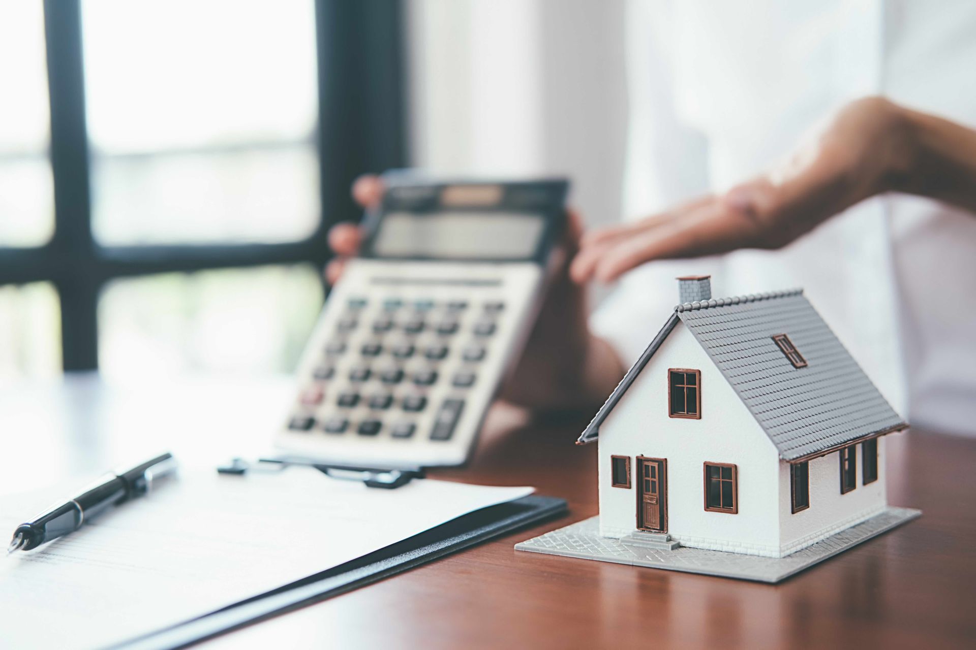 Mini house model on a desk with calculator, pen, and clipboard in an office setting