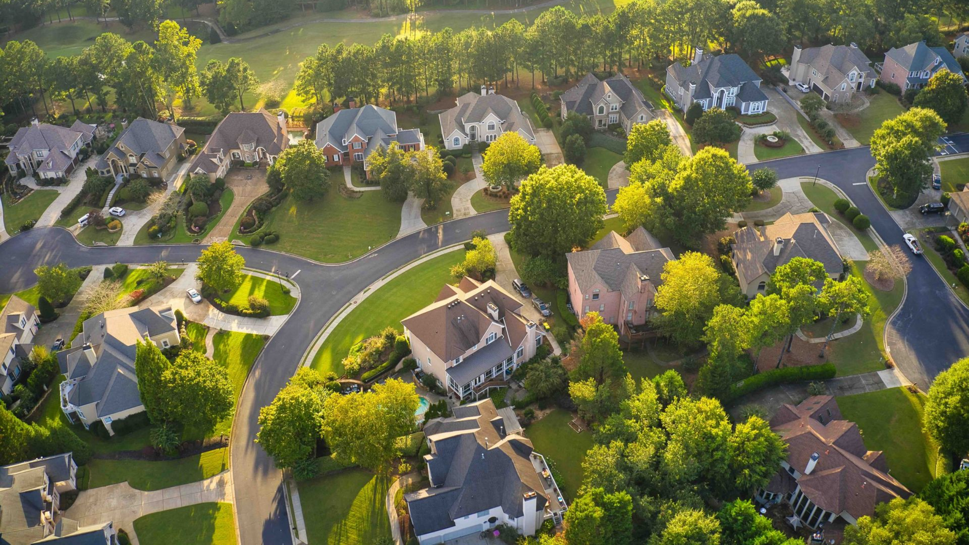 Aerial view of a suburban neighborhood with houses, trees, and streets on a sunny day.