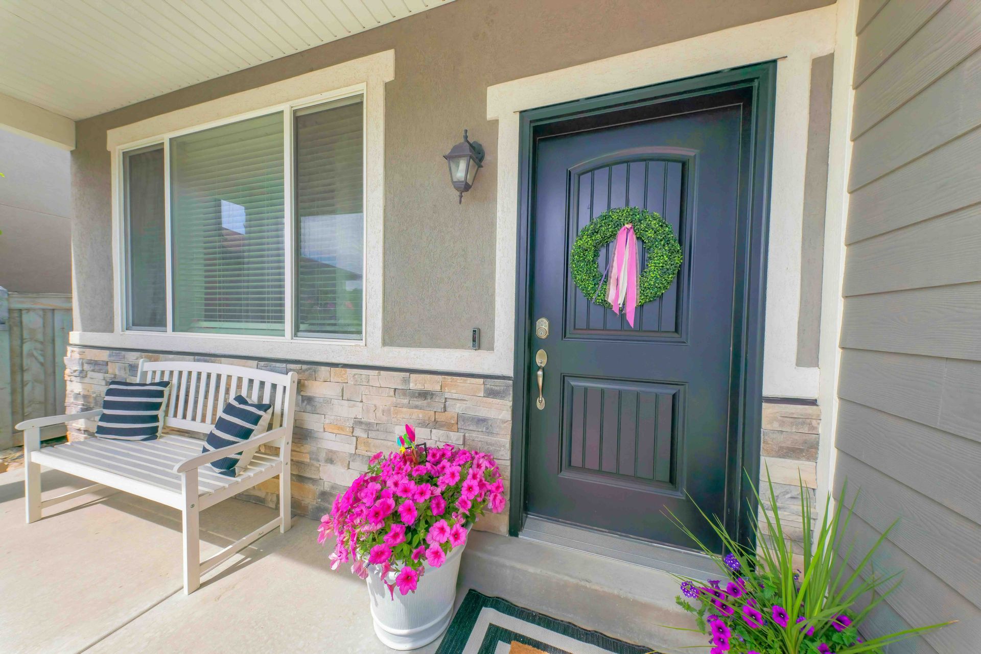 A porch with a bench , flowers and a wreath on the door.