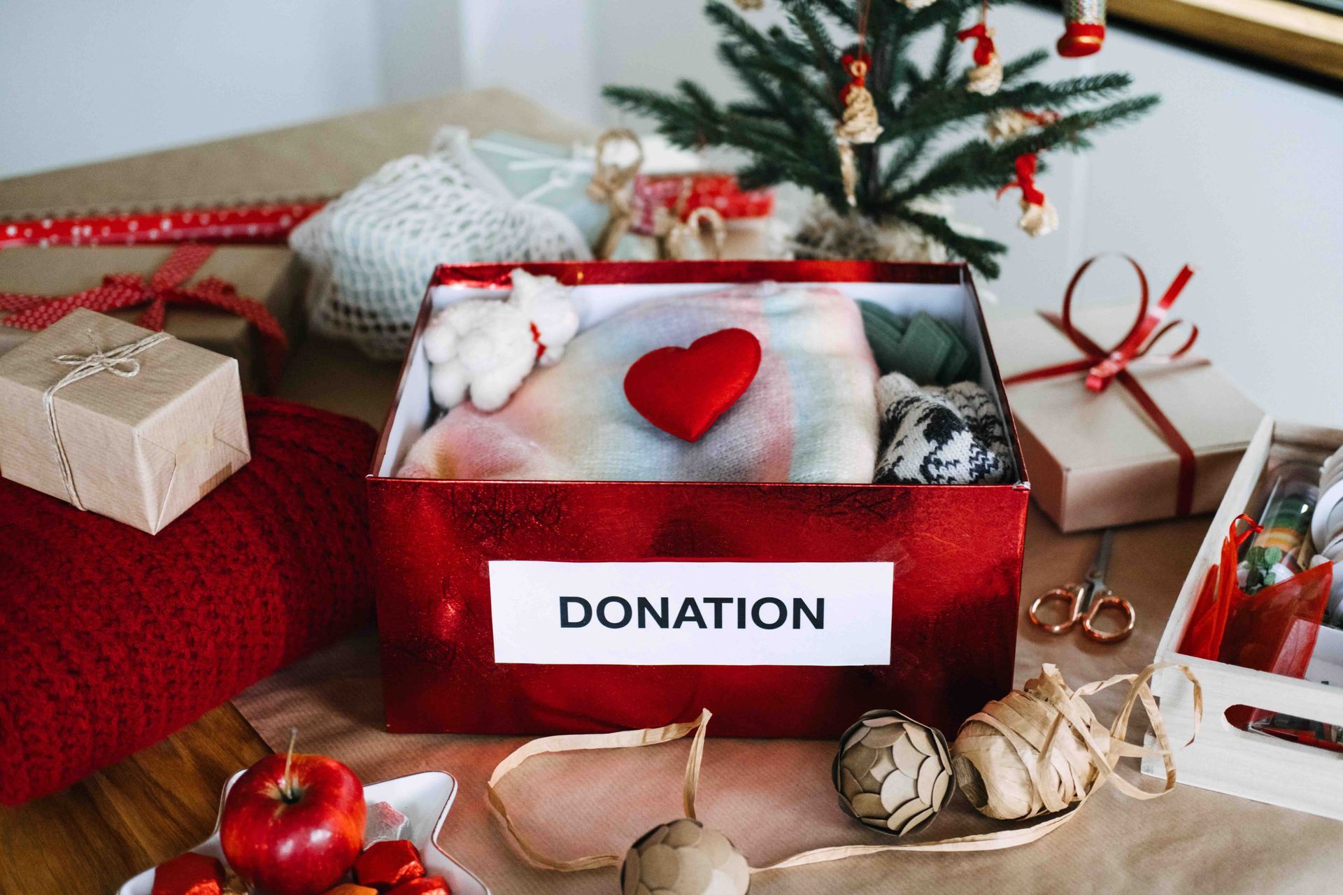 Donation box with red heart, surrounded by wrapped gifts and holiday decorations
