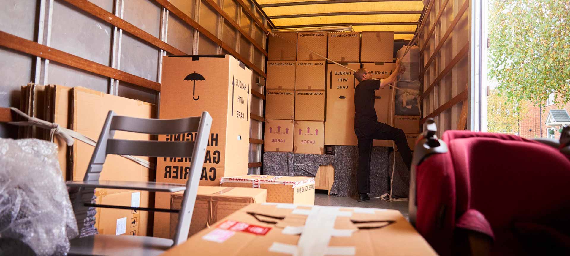Truck interior filled with boxes, furniture, and a red chair in a moving scene