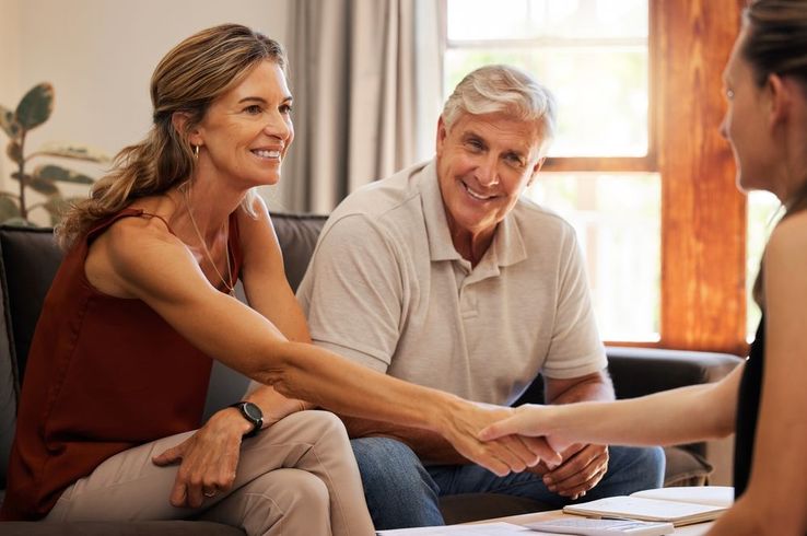 A man and woman are shaking hands with a woman while sitting on a couch.