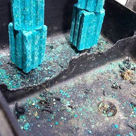 Turquoise paint flakes and debris around two turquoise plastic columns on a dark surface
