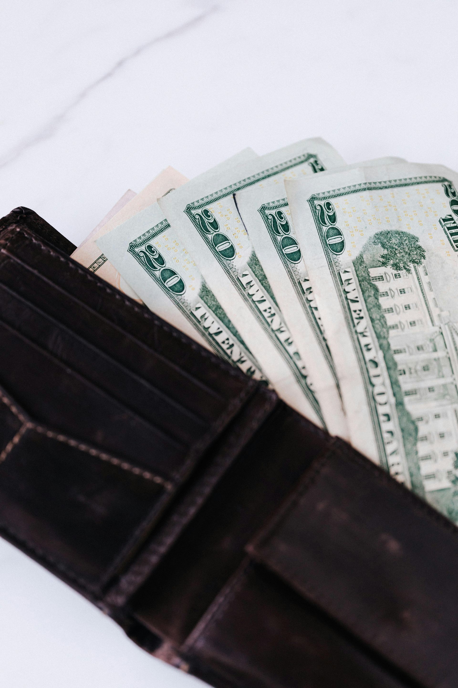 Brown leather wallet with a fan of fifty dollar bills partially visible.