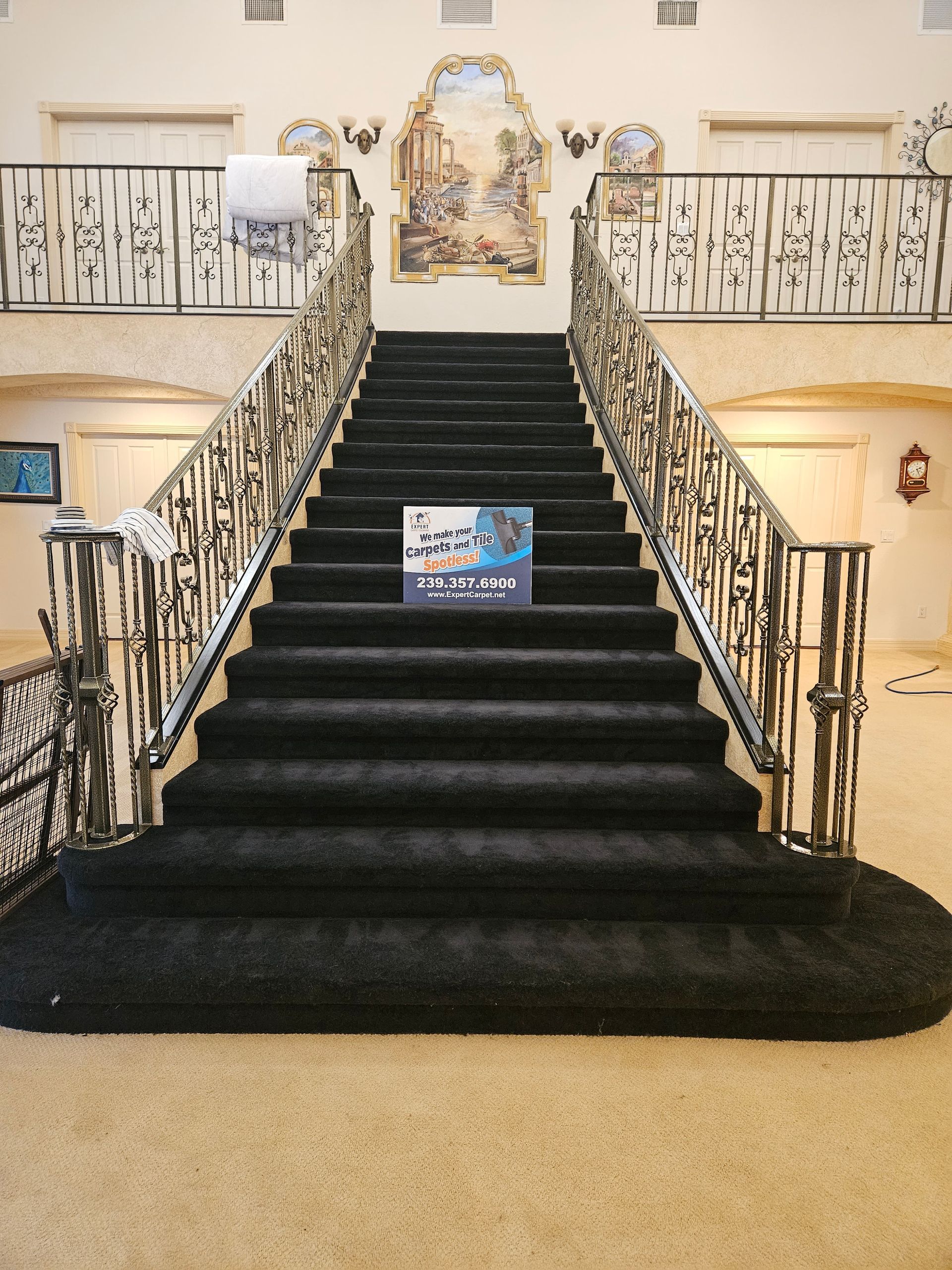 Grand staircase with black carpet, ornate railings, and a decorative mural at the top.