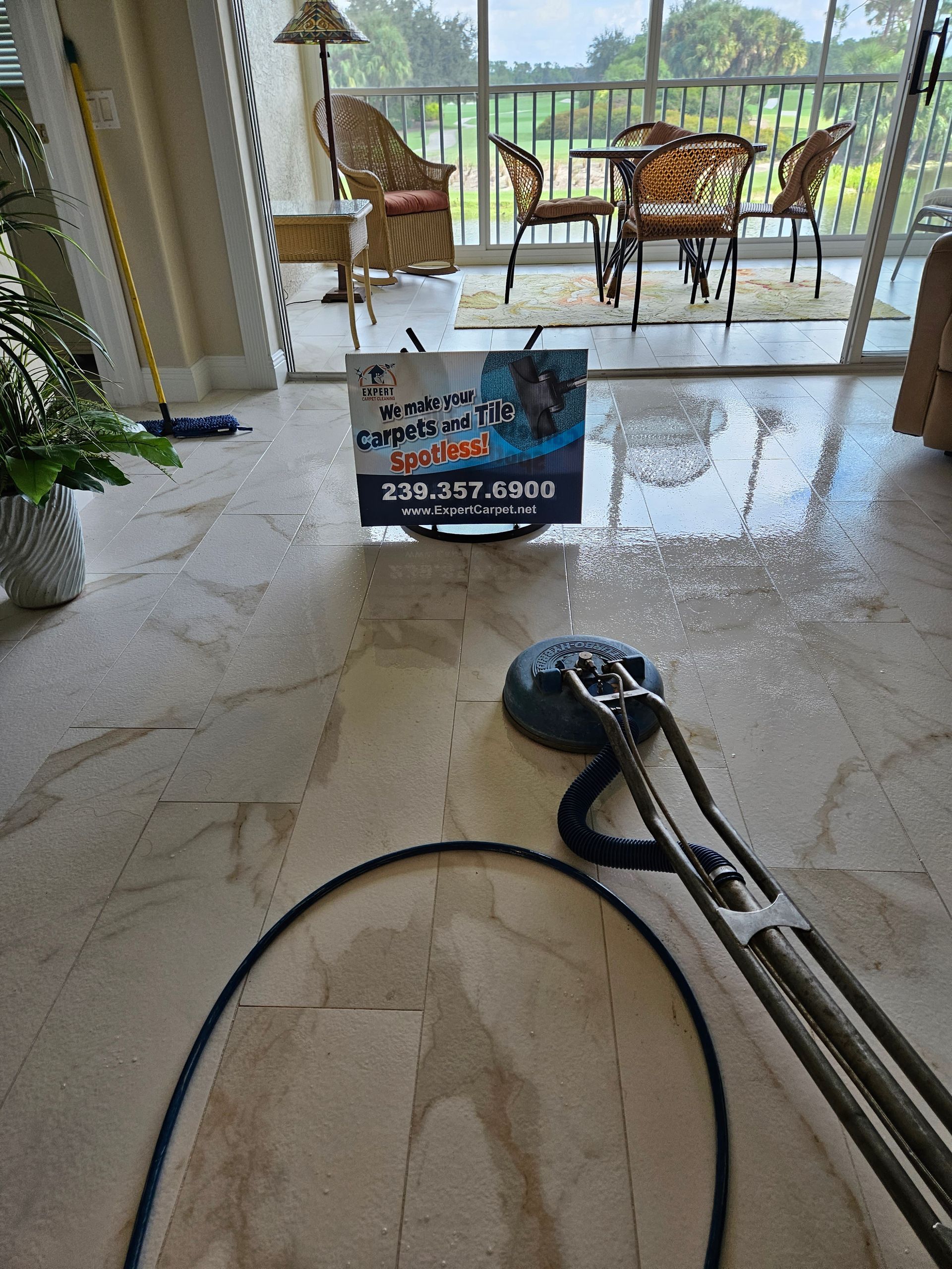 Vacuum cleaner in a bright tiled patio room with a sign and outdoor chairs beyond the glass doors