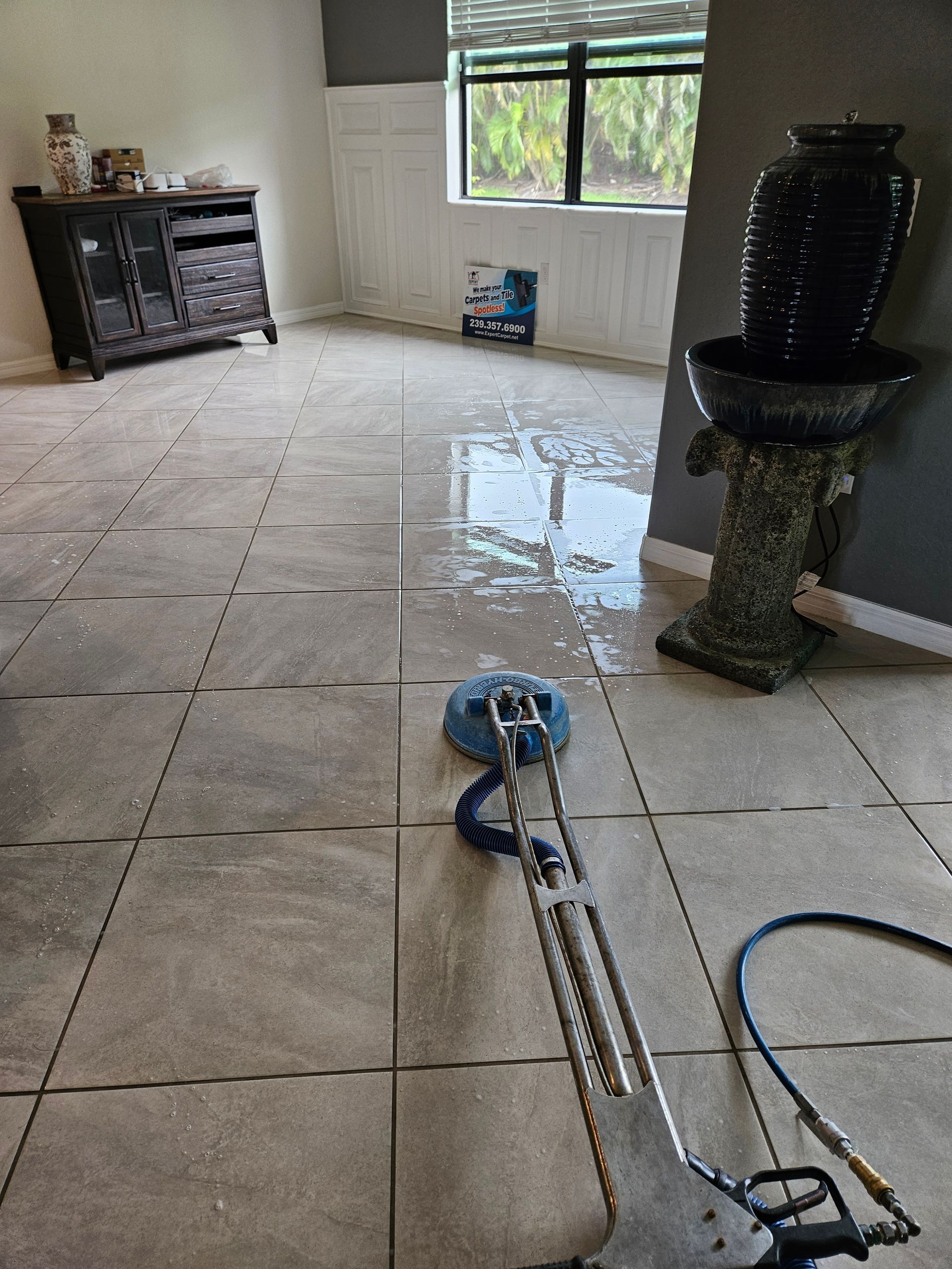Large tiled room with a wet floor being cleaned by a floor buffer, cabinets and a window in the background
