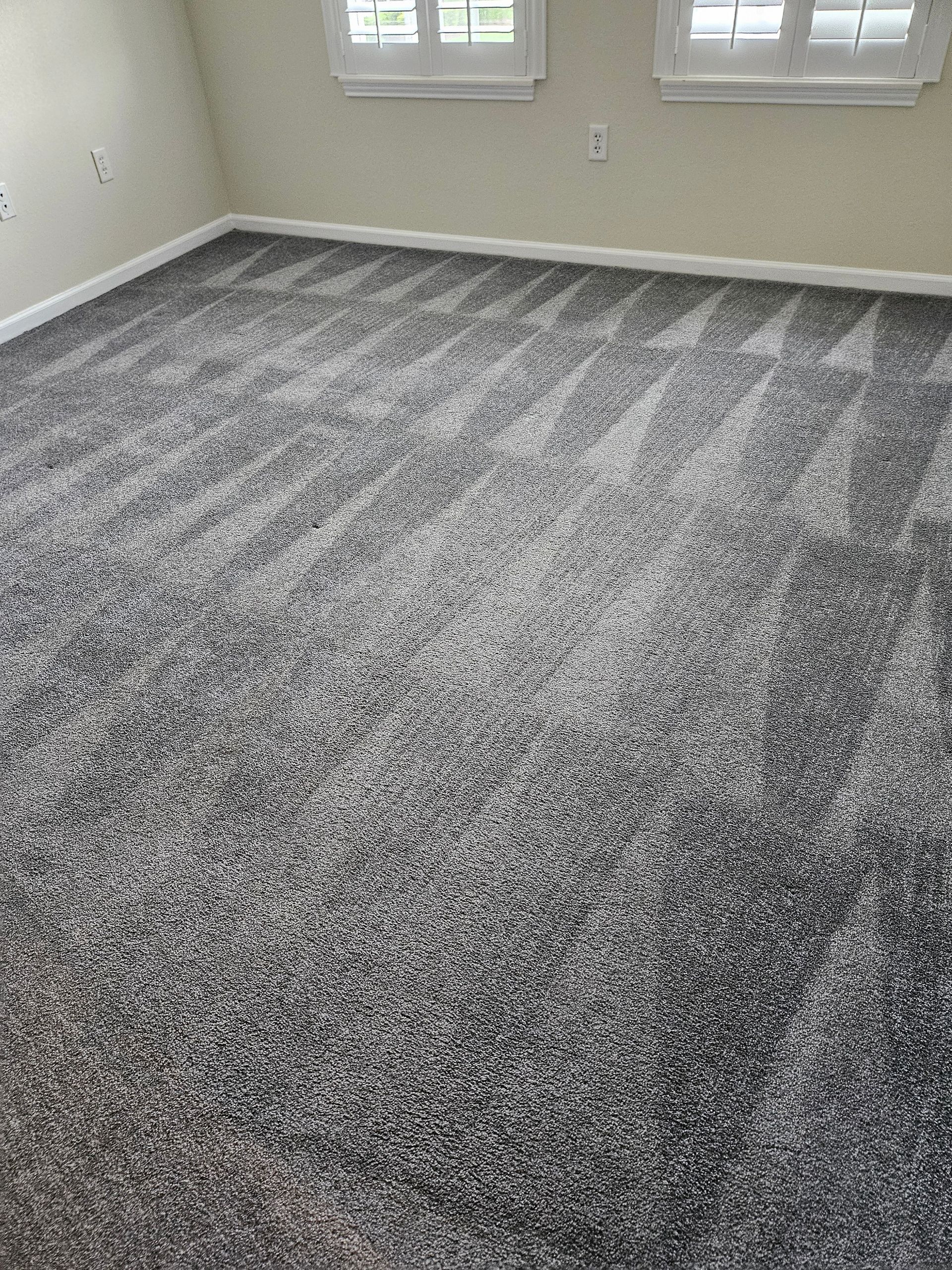 Empty room with gray carpet and two windows letting in natural light