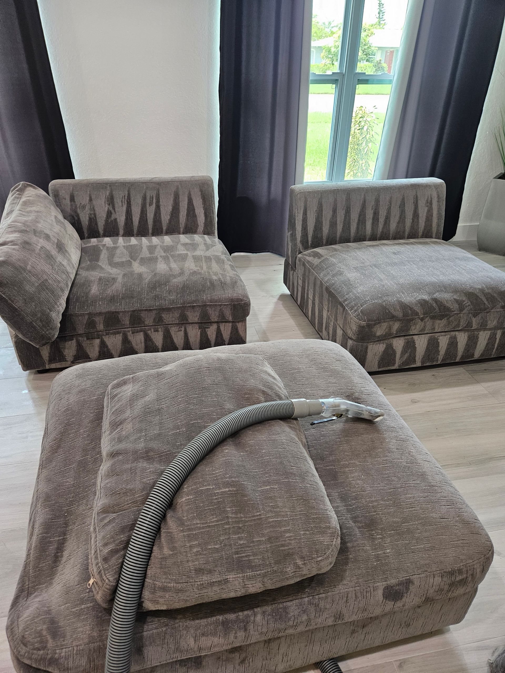 Gray patterned floor cushions and an upholstered chair by a window; a hose lies across the front cushion.