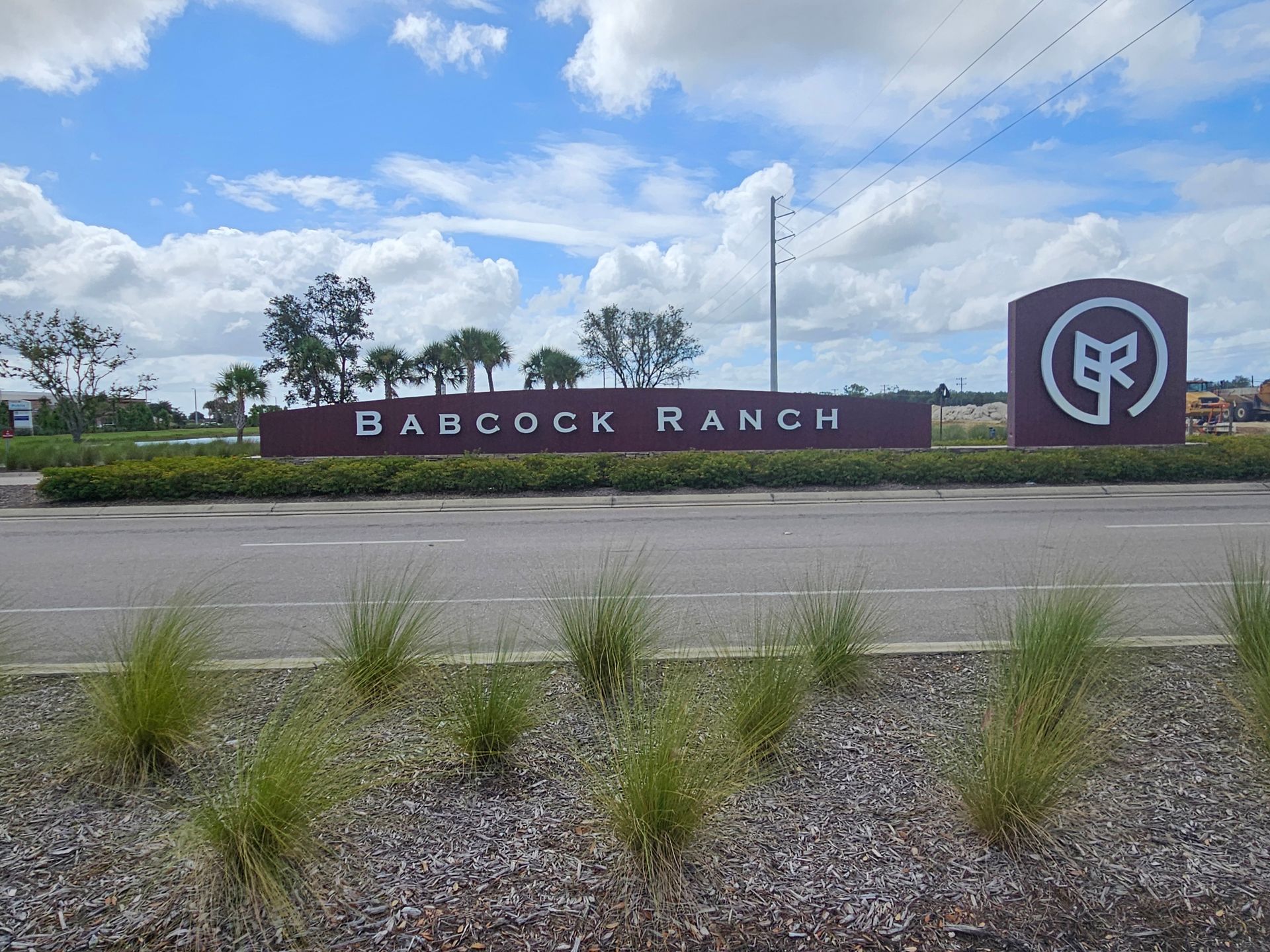Babcock Ranch entrance sign with logo beside a road under a cloudy sky.