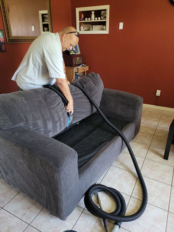 Person vacuuming a gray couch in a living room with red walls and tiled floor.