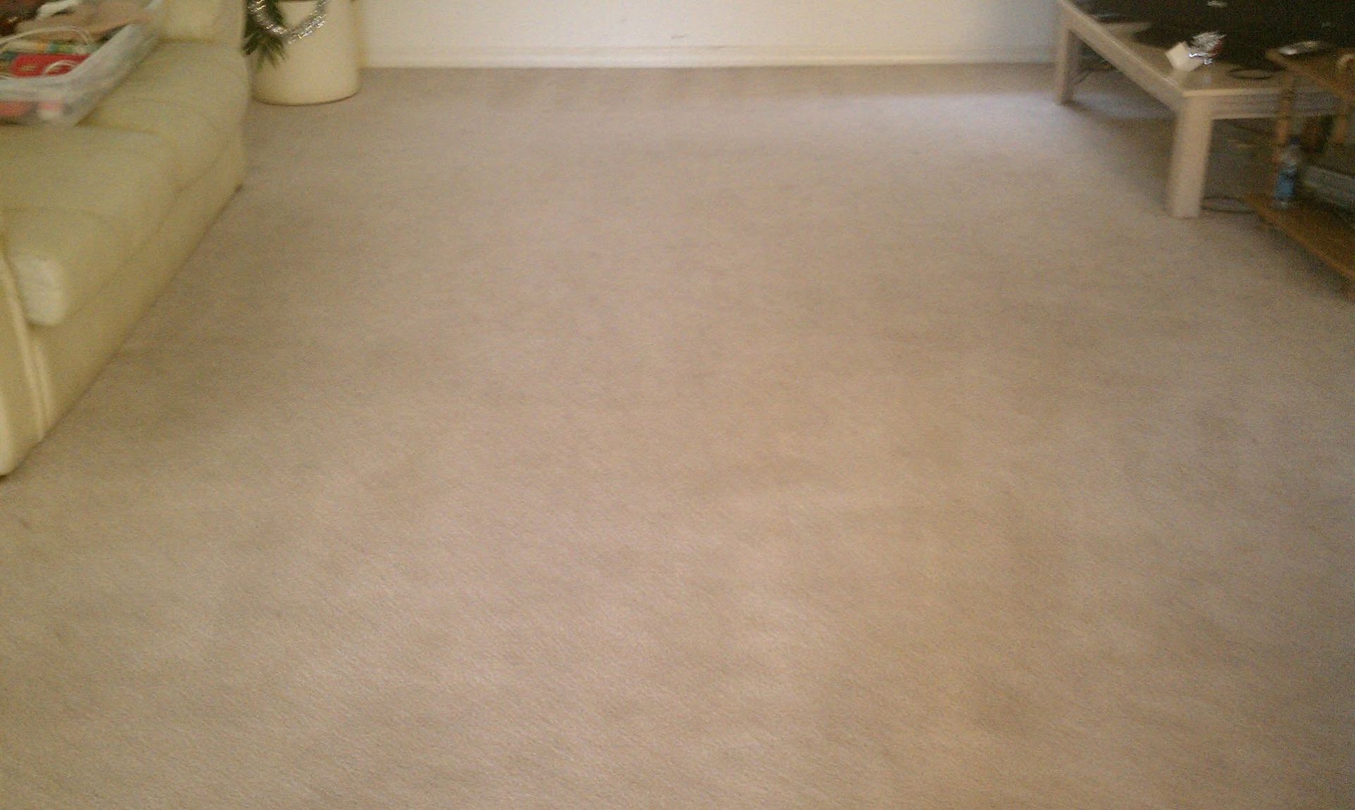 Empty beige-carpeted living room with a sofa on the left and a small table on the right