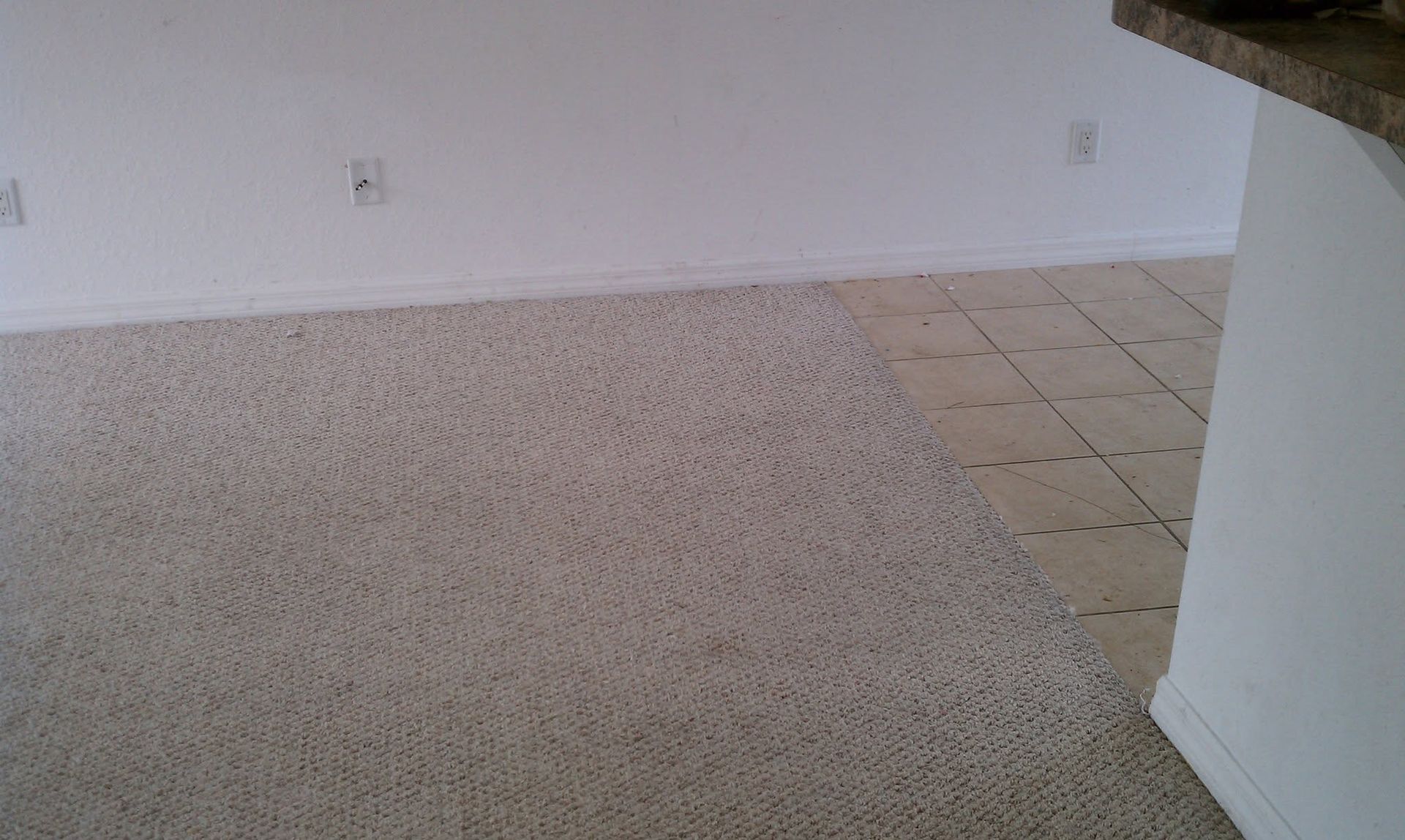 Empty carpeted room with tiled entryway and white walls