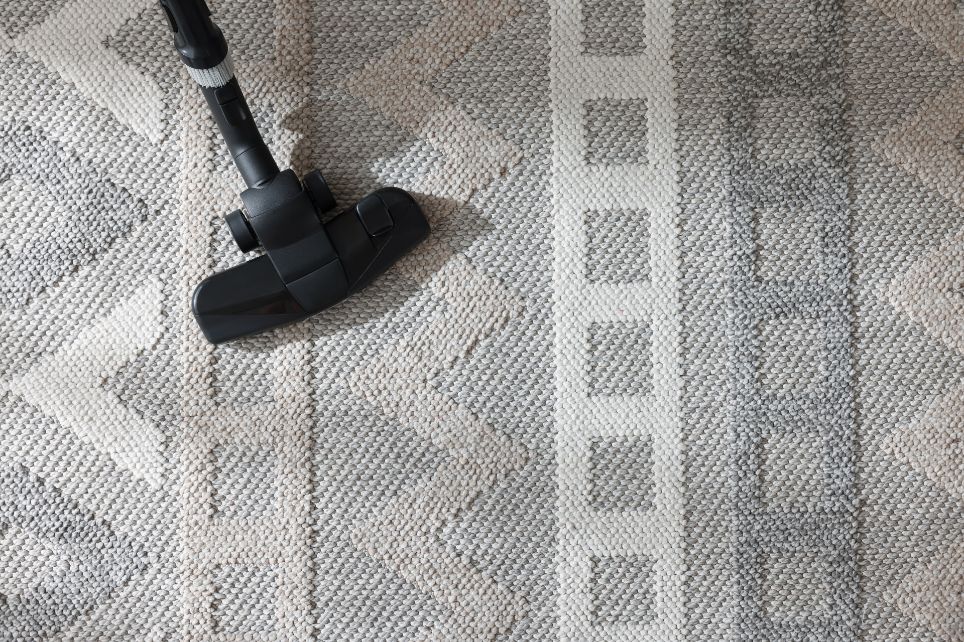 A black vacuum cleaner head on a patterned gray carpet with a light-striped runner beside it